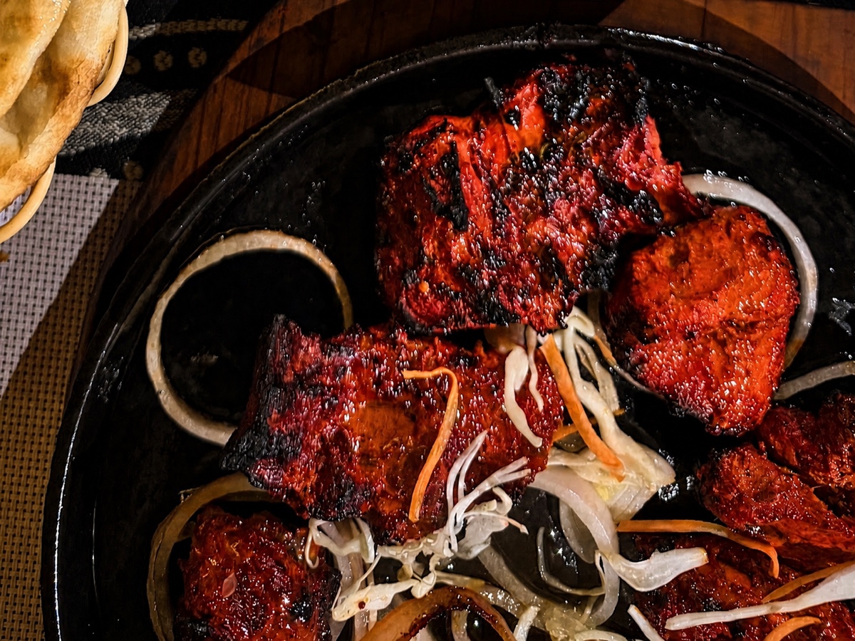 Sizzling plate of char-red tandoori chicken with onion rings