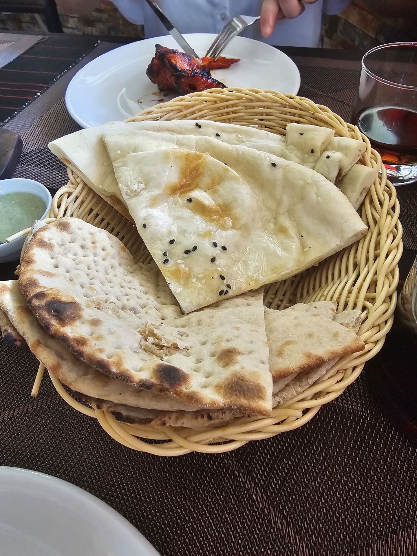 Basket of blistered naan and roti with green chutney and tandoori chicken behind