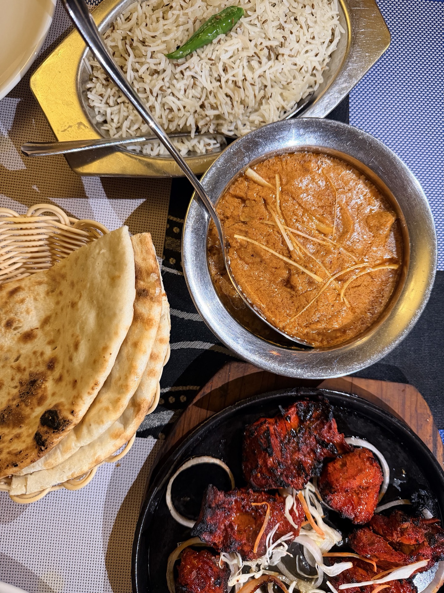 Top-down table spread of karahi, zeera rice, naan basket and sizzling tandoori chicken